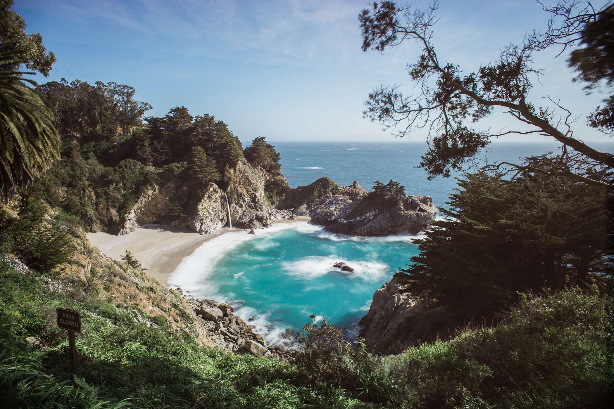 The waterfall of McWay falls over the turquoise beach on a clear day.