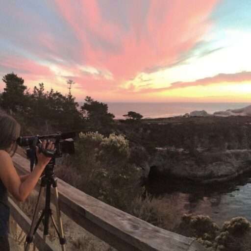 Light fill the sky over Point Lobos, Monterey County. We see the effects of light at sunset as the sky changes to red. Marlene studies the effects through the camera lens.